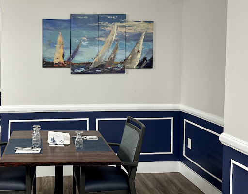 A cozy dining area featuring a wooden table, comfortable chairs, and a vibrant painting of sailboats on a blue wall.