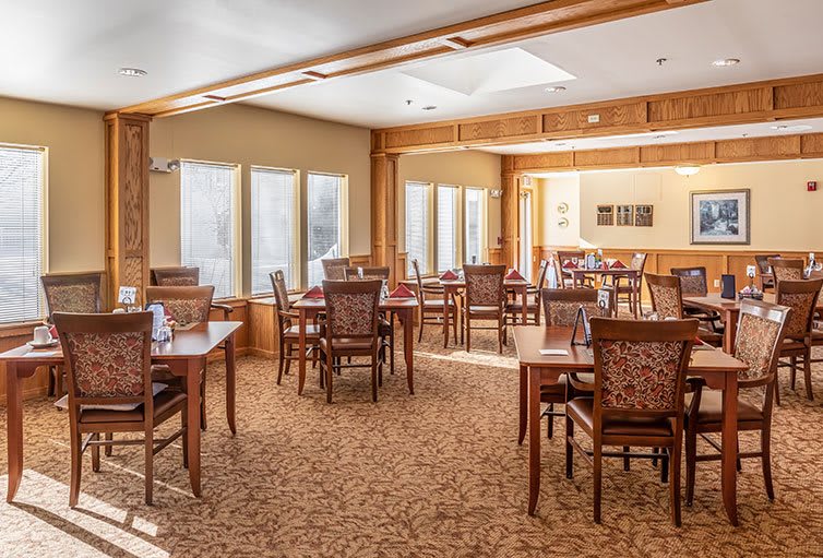 A spacious dining room with wooden tables and chairs, illuminated by natural light.