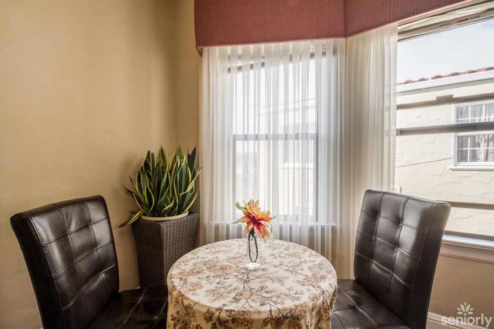 A cozy corner with a round table, two chairs, a potted plant, and a vase with flowers by the window.