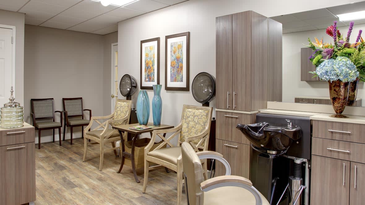 A cozy salon interior featuring chairs, hairdryers, decorative vases, and artwork on the walls.