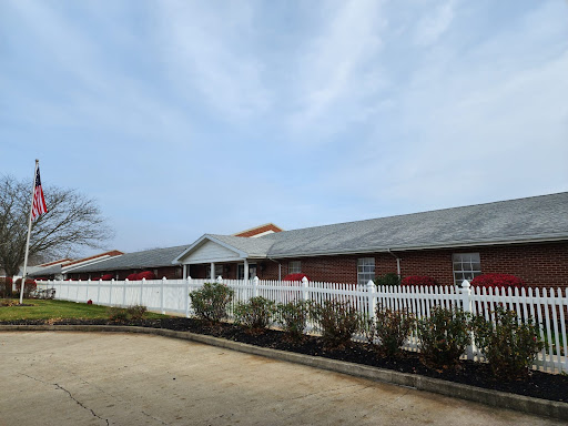 A serene view of a brick building surrounded by a white picket fence against a cloudy sky.