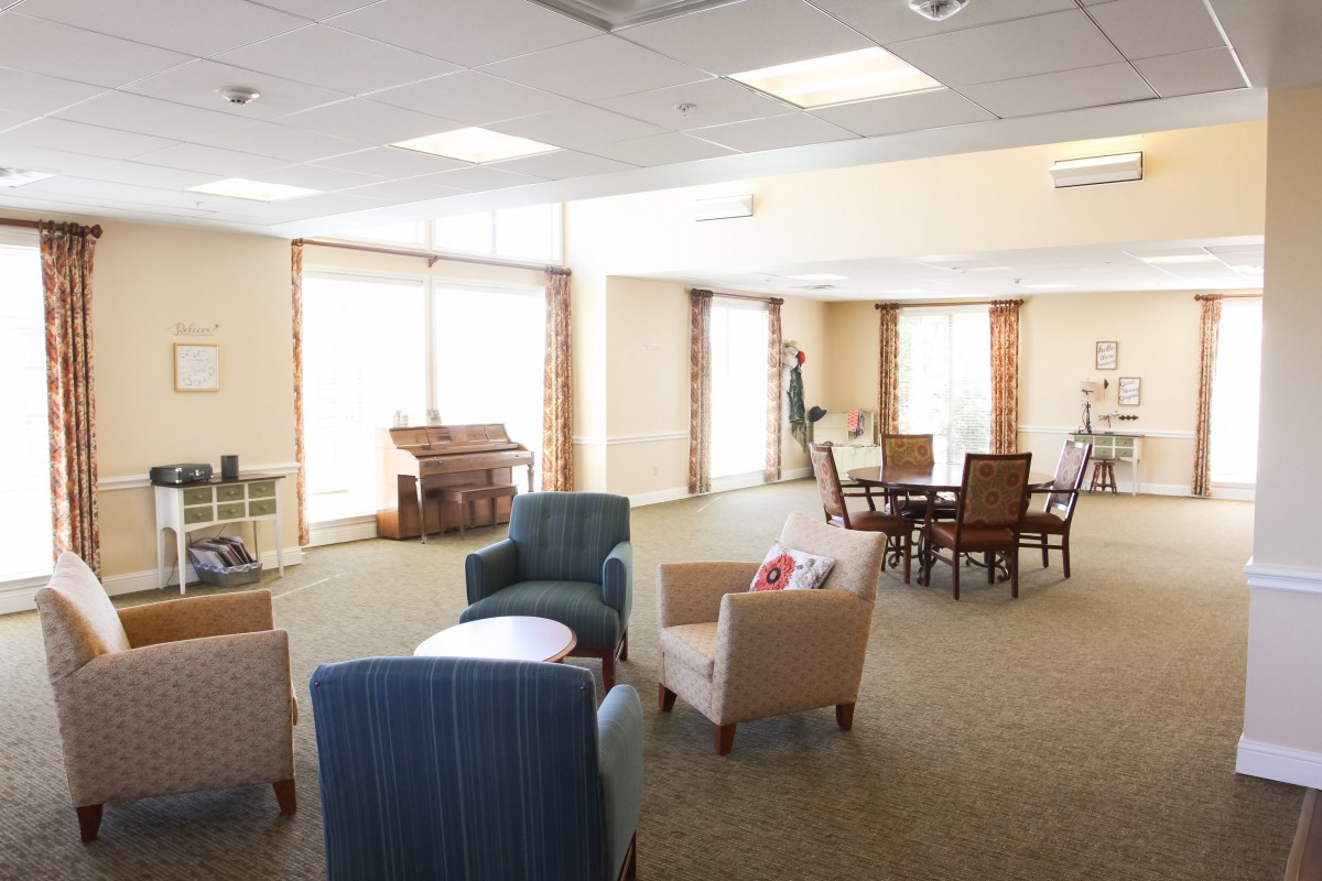 A spacious community room with comfortable seating and large windows, illuminated by ceiling lights.