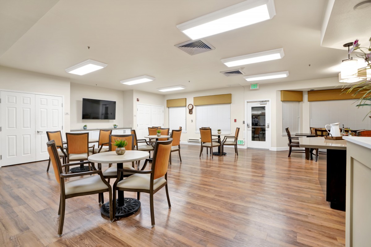 A modern dining area with wood flooring, tables, and chairs, featuring a television on the wall.