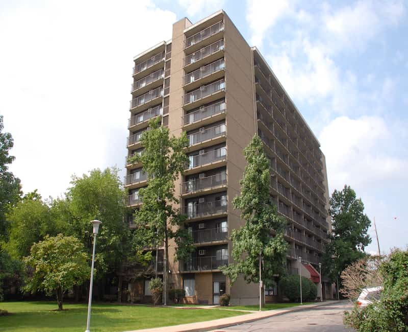 A high-rise apartment building surrounded by trees on a clear day.