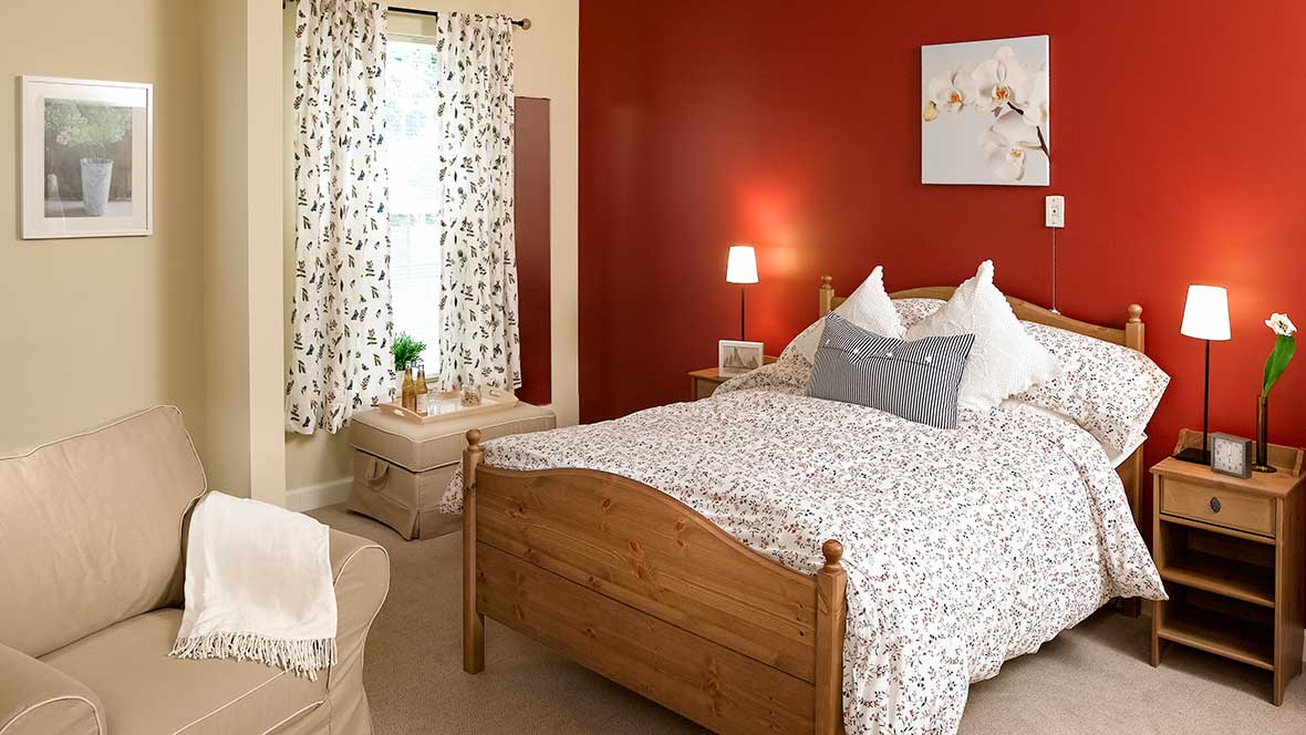 A cozy bedroom with a wooden bed and red accent wall.