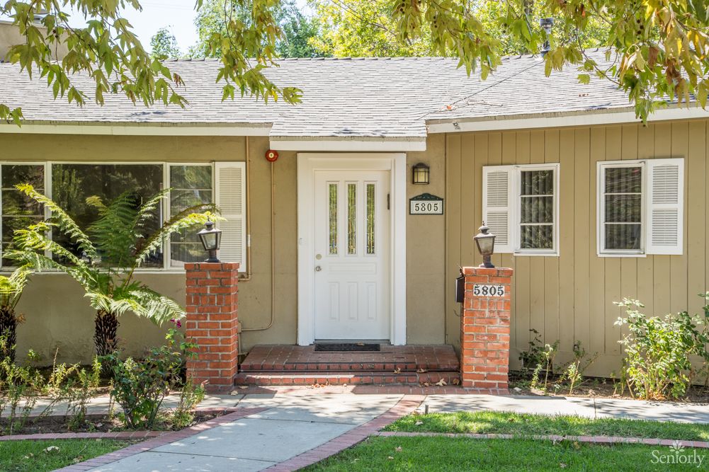 A cozy residential house with a white front door, surrounded by a yard and brick pillars.
