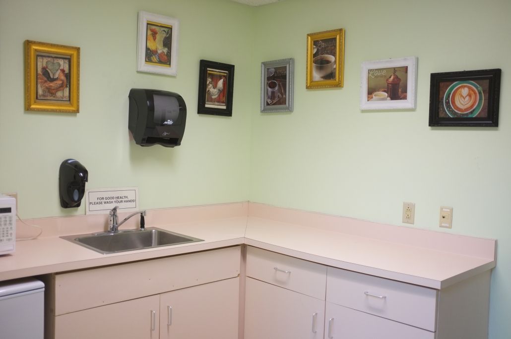 A clean veterinary exam room with a sink, cabinets, and framed pictures on the walls.