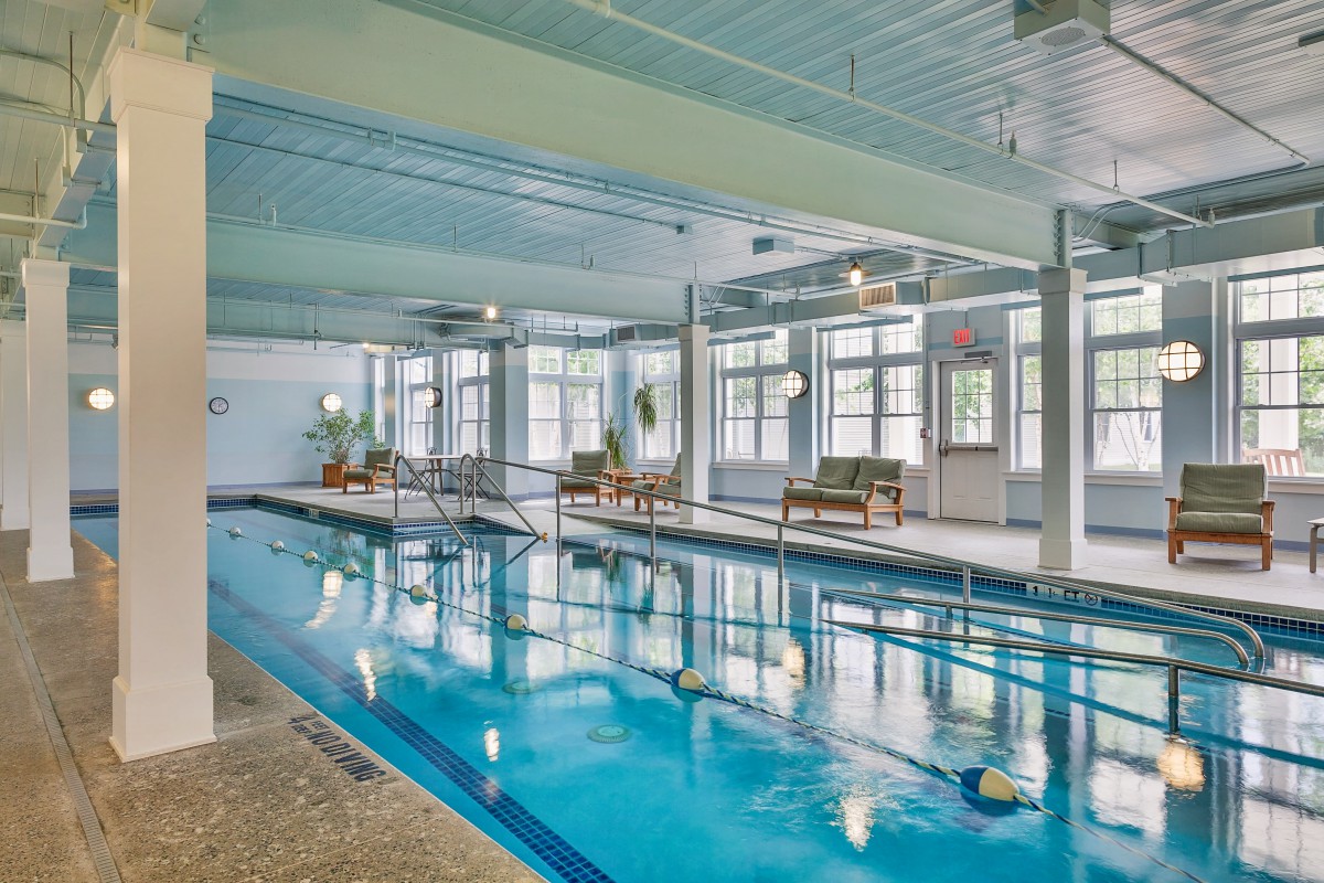 An indoor swimming pool with lounge chairs and large windows.