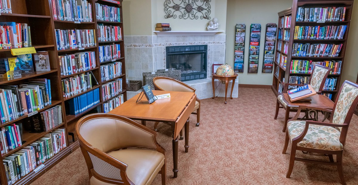 A cozy library corner with bookshelves, a fireplace, and comfortable seating.