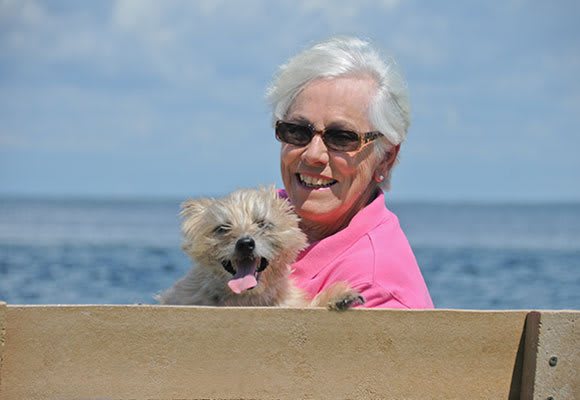 A woman wearing sunglasses enjoys a sunny day at the beach with her dog.
