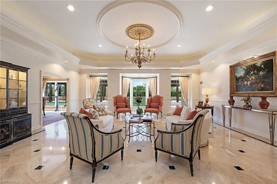 A luxurious living room featuring elegant decor with a central chandelier and stylish armchairs on a marble floor.