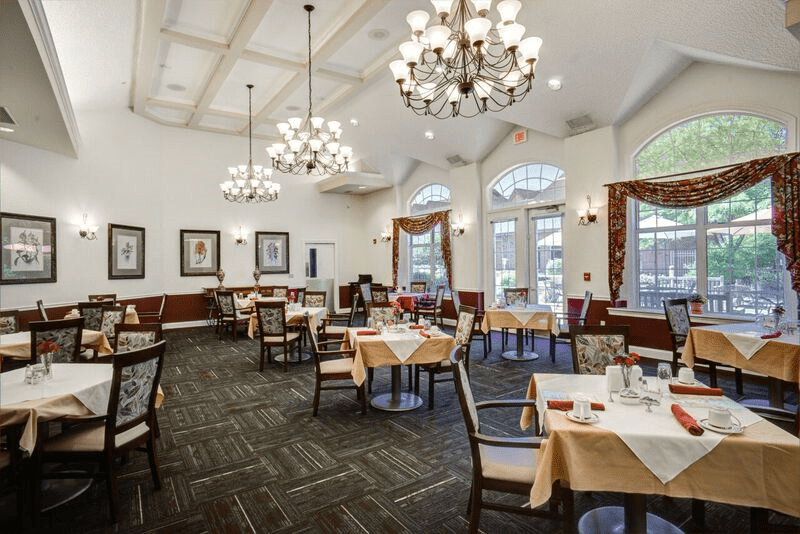 An elegant dining room with chandeliers, neatly arranged tables, and chairs.
