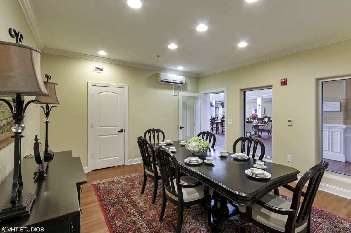 A well-lit dining room featuring a dark wooden table with six chairs and a decorative rug.