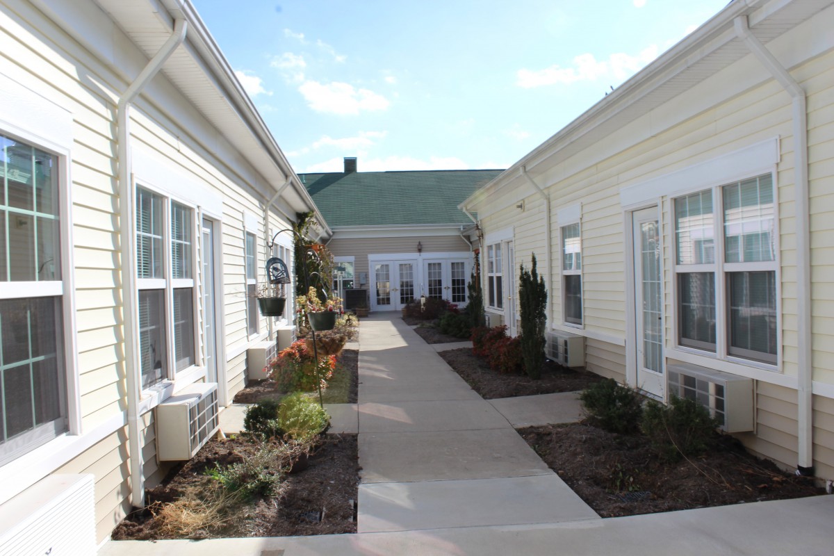 A view of a pathway between two buildings with neatly maintained landscaping and a clear sky above.