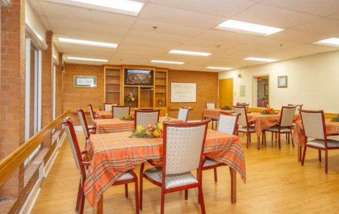 A cozy dining room with neatly arranged tables and chairs, featuring orange tablecloths and a television.