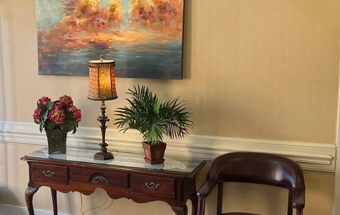 A stylish interior setup featuring a decorative table with a lamp, plants, and a painting on the wall.