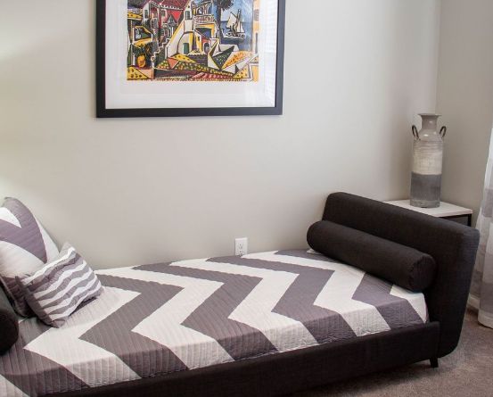 A modern bedroom with a zigzag-patterned daybed and framed artwork on the wall.
