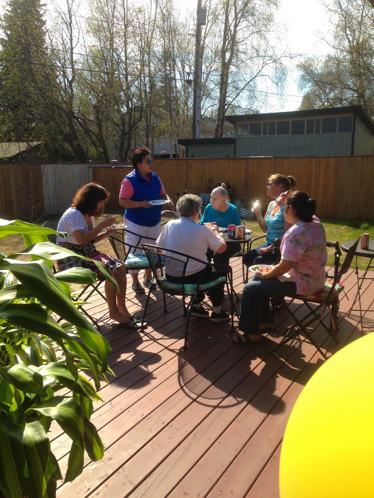 A group of people enjoying a sunny gathering on a wooden deck.