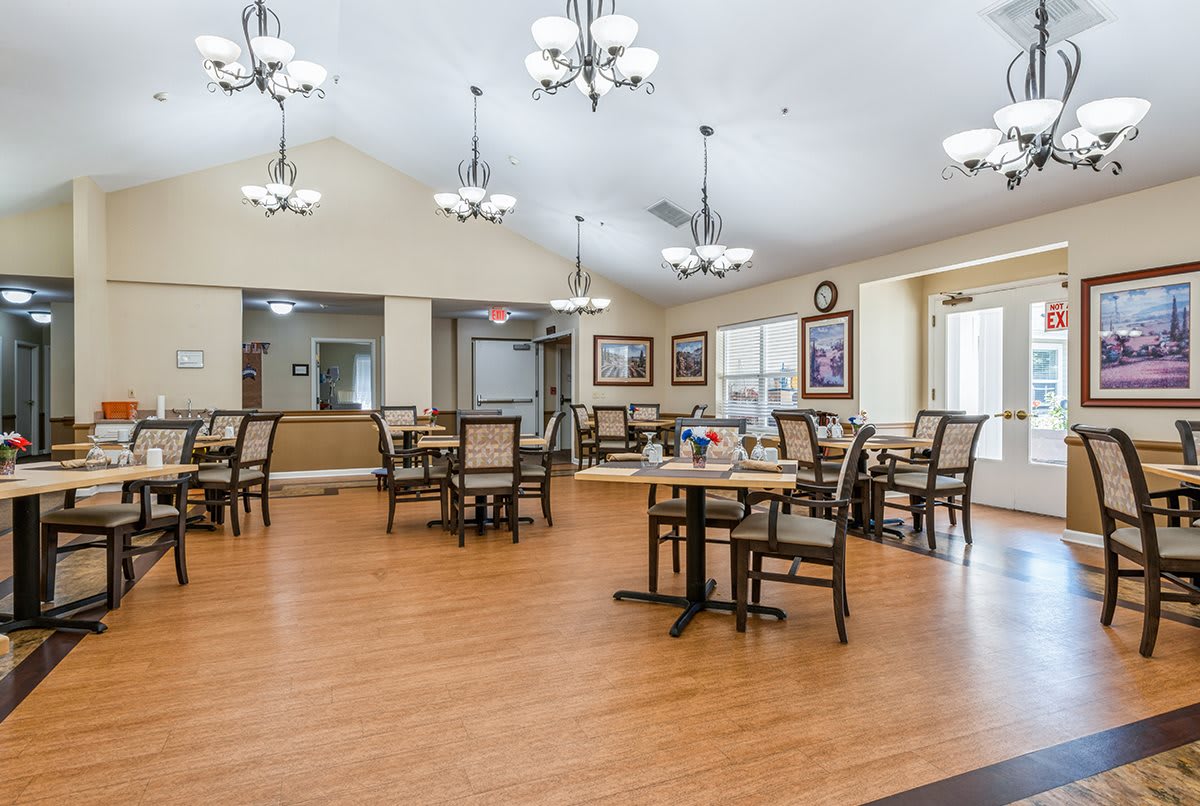 A spacious dining area with wooden floors, tables and chairs arranged neatly under elegant chandeliers.