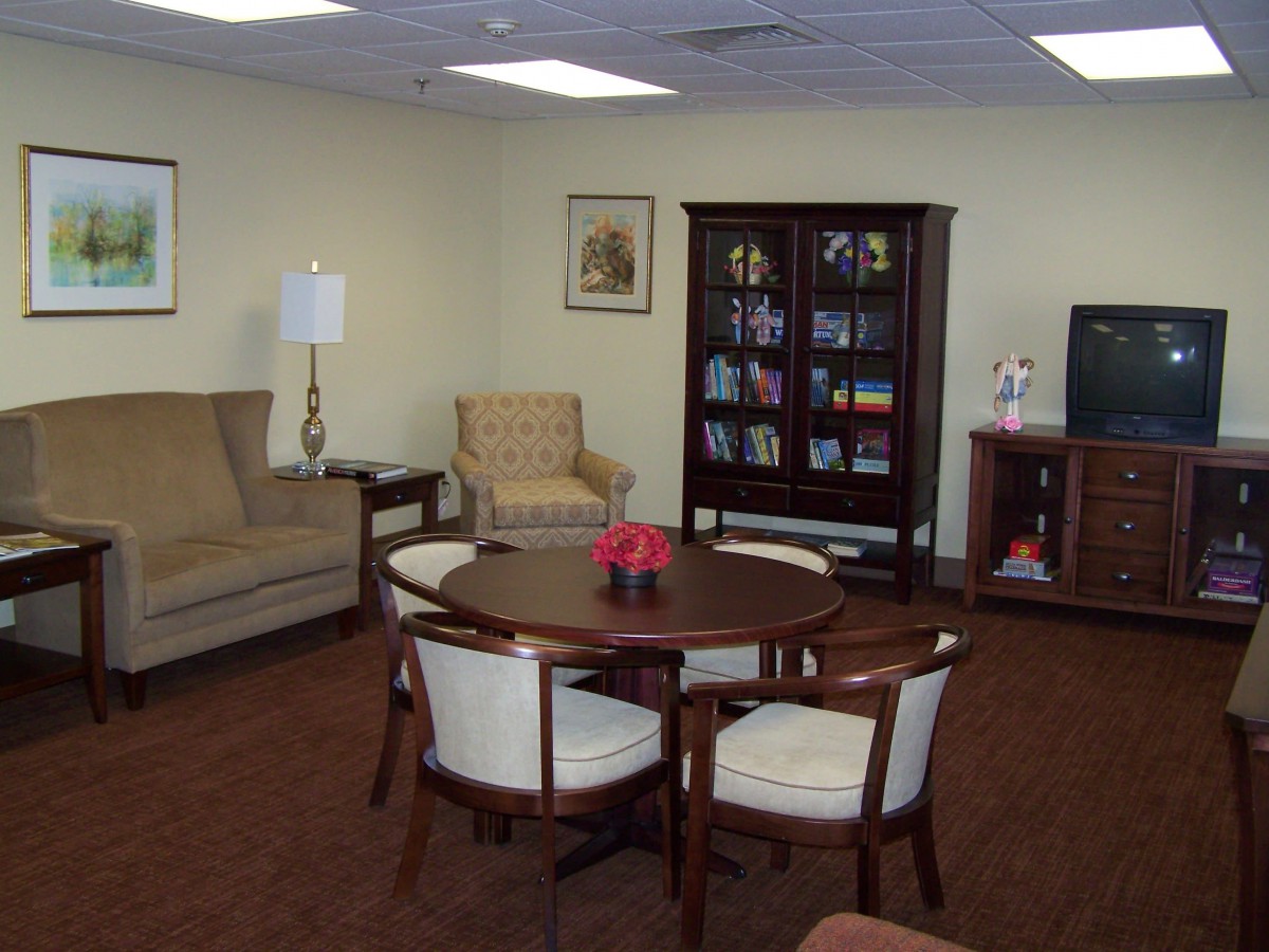A cozy living room with a sofa, chairs around a table, a bookshelf, and a television.