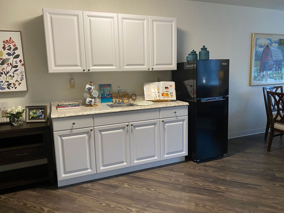 A small kitchen area featuring white cabinets, a countertop with appliances, and a black refrigerator.