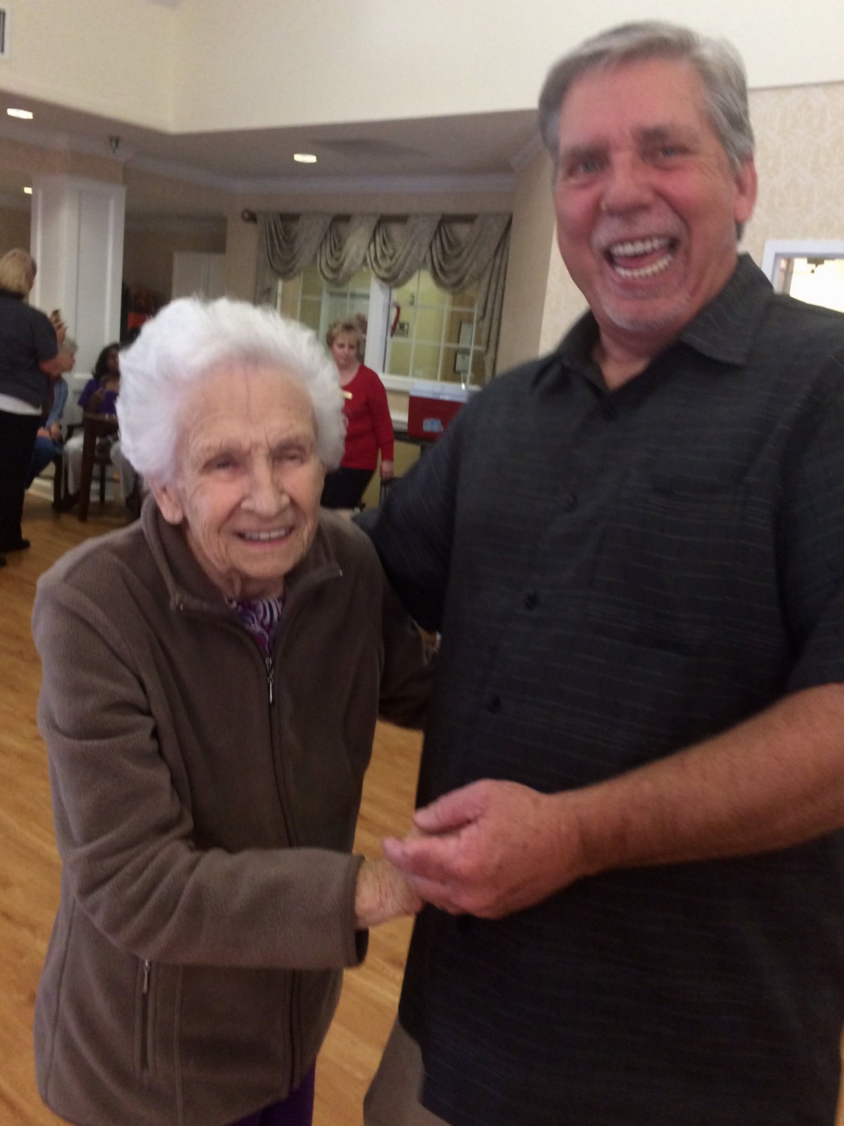 An elderly woman and a man share a joyful moment indoors.