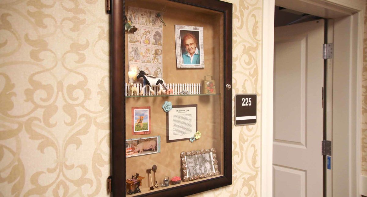 A display case containing a collection of memorabilia including a photograph, decorative items, and a room number sign on the wall.