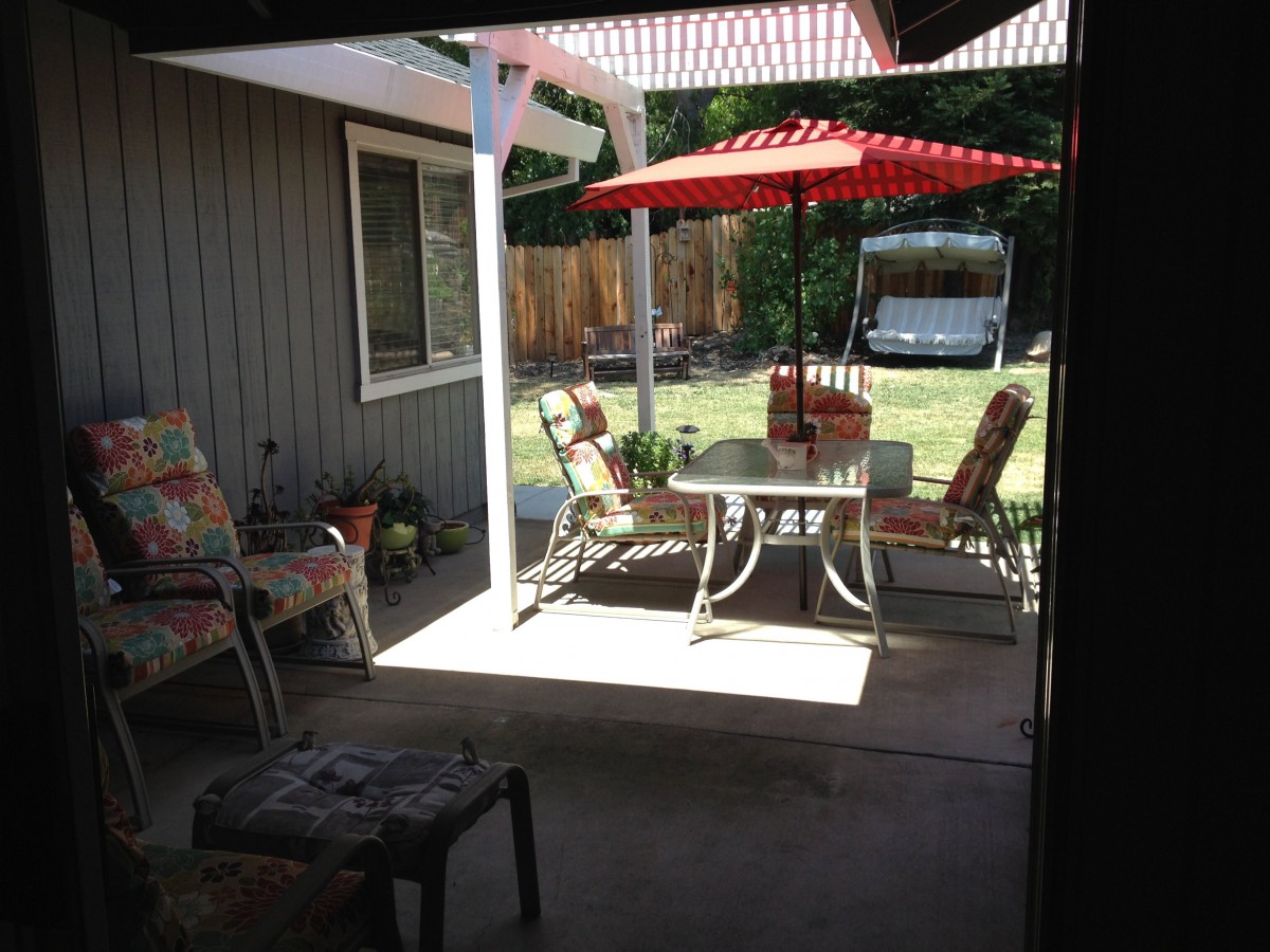 A sunny backyard patio with outdoor furniture and a red umbrella.