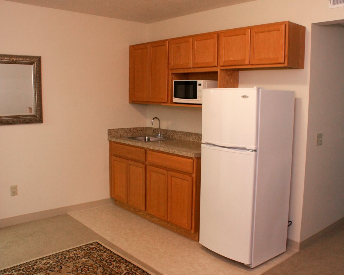 A small kitchen area with wooden cabinets, a refrigerator, and a microwave.