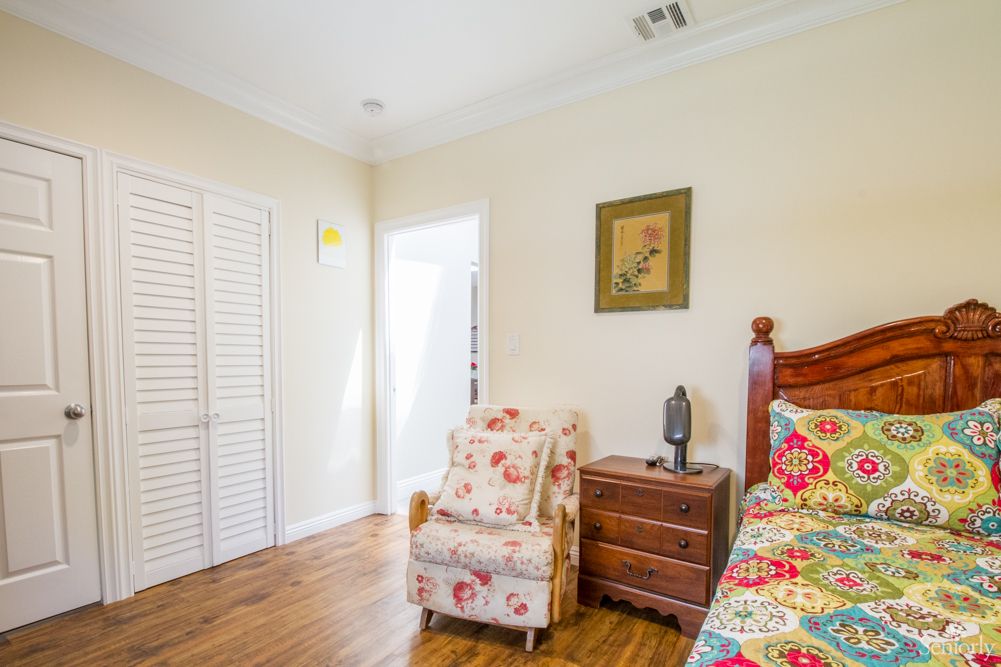 A cozy bedroom featuring a floral armchair, wooden bed, and decorative painting.