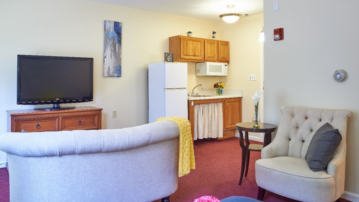 A cozy living space with a small kitchen area, featuring a refrigerator and microwave.