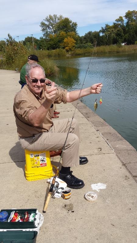 A man excitedly shows off a small catch while fishing by a lake.