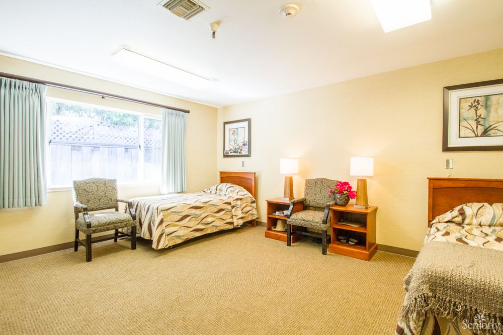 A well-lit bedroom with cozy furnishings including a bed, chairs, and lamps.