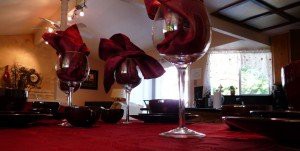 An elegant table setting featuring wine glasses with red napkins, set in a warmly lit dining room.