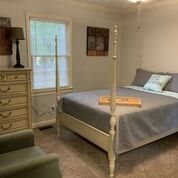 A cozy bedroom with a four-poster bed, a dresser, and a lamp beside a window.