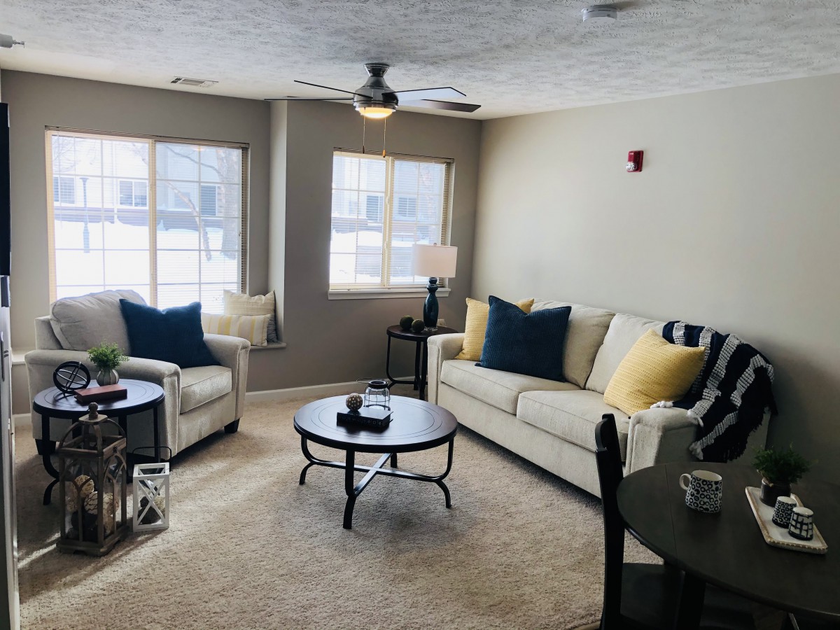 A cozy living room with neutral tones, featuring a sofa and armchairs, centered around a round coffee table.