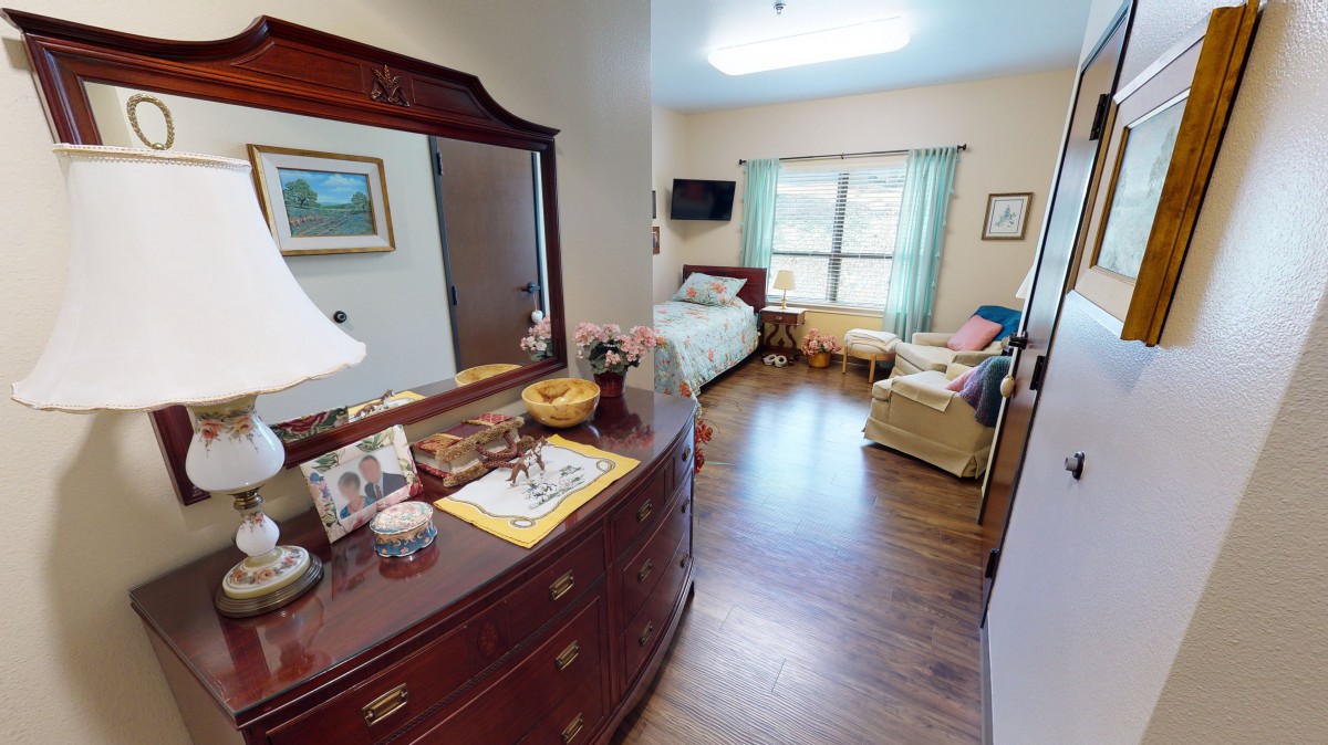 A cozy bedroom featuring a bed, a comfortable chair, and a dresser with decorative items.