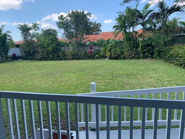 A backyard view with a grassy lawn and surrounding trees, seen from a deck.