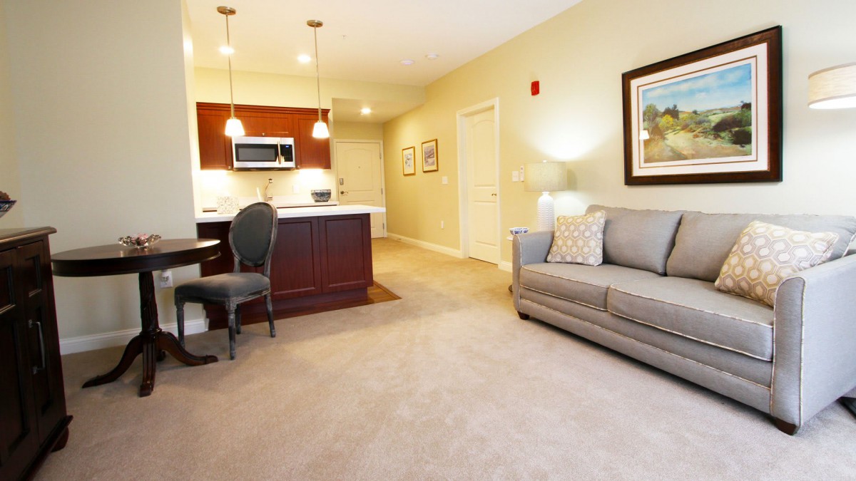 A modern living room with an integrated kitchen and dining area, featuring stylish furniture and warm lighting.