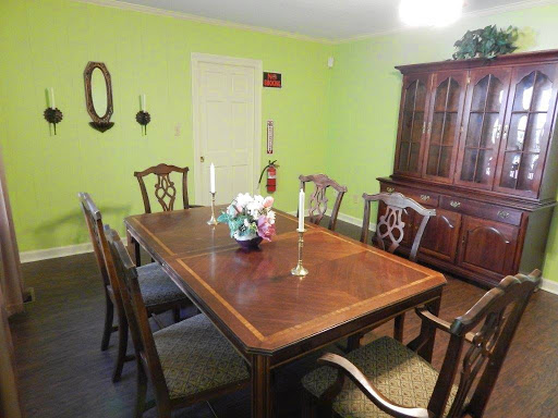 A cozy dining room featuring a wooden table and chairs, accented by green walls and a beautiful floral centerpiece.