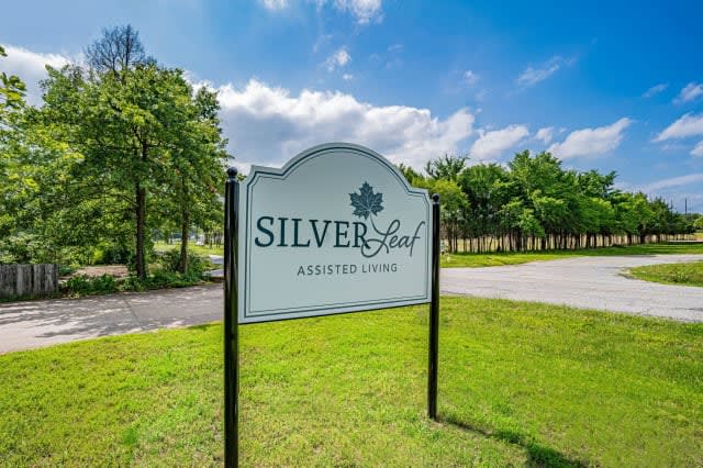 A sign for Silver Leaf in Addison, Texas, stands outdoors against a backdrop of trees and a blue sky.