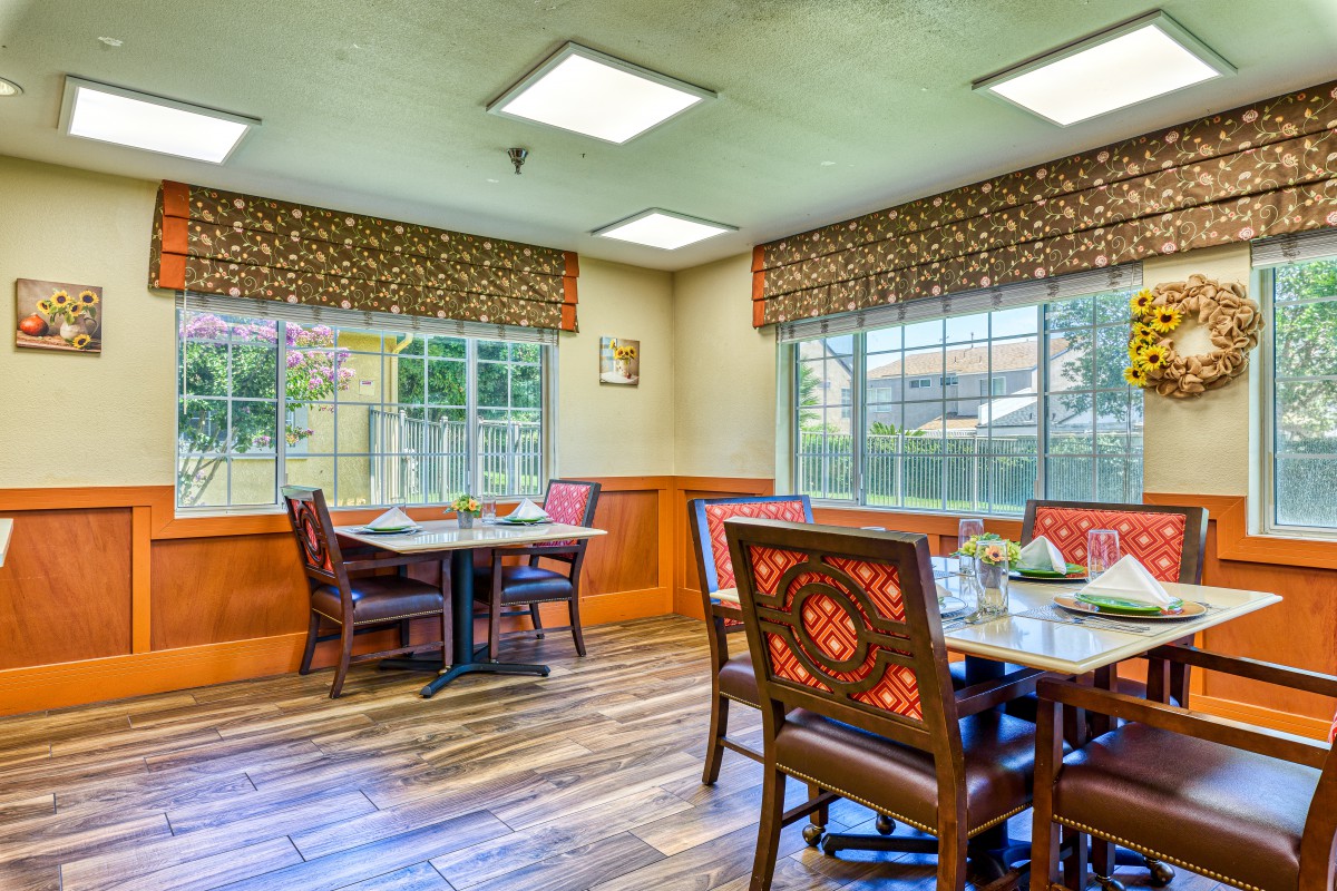 A cozy dining room with wooden floors, tables, chairs, and large windows.