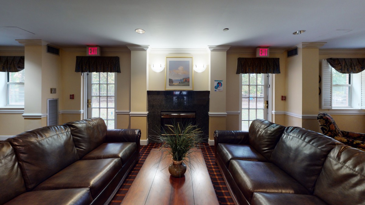 A cozy living room with leather sofas, a wooden coffee table, and a central fireplace flanked by large windows.