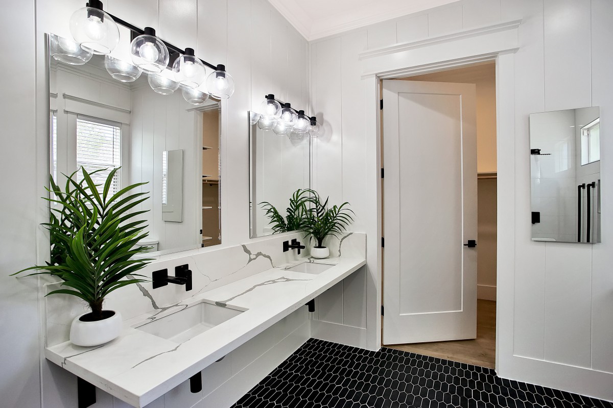 A modern bathroom featuring a double sink, large mirror, and stylish lighting, complemented by indoor plants and black floor tiles.