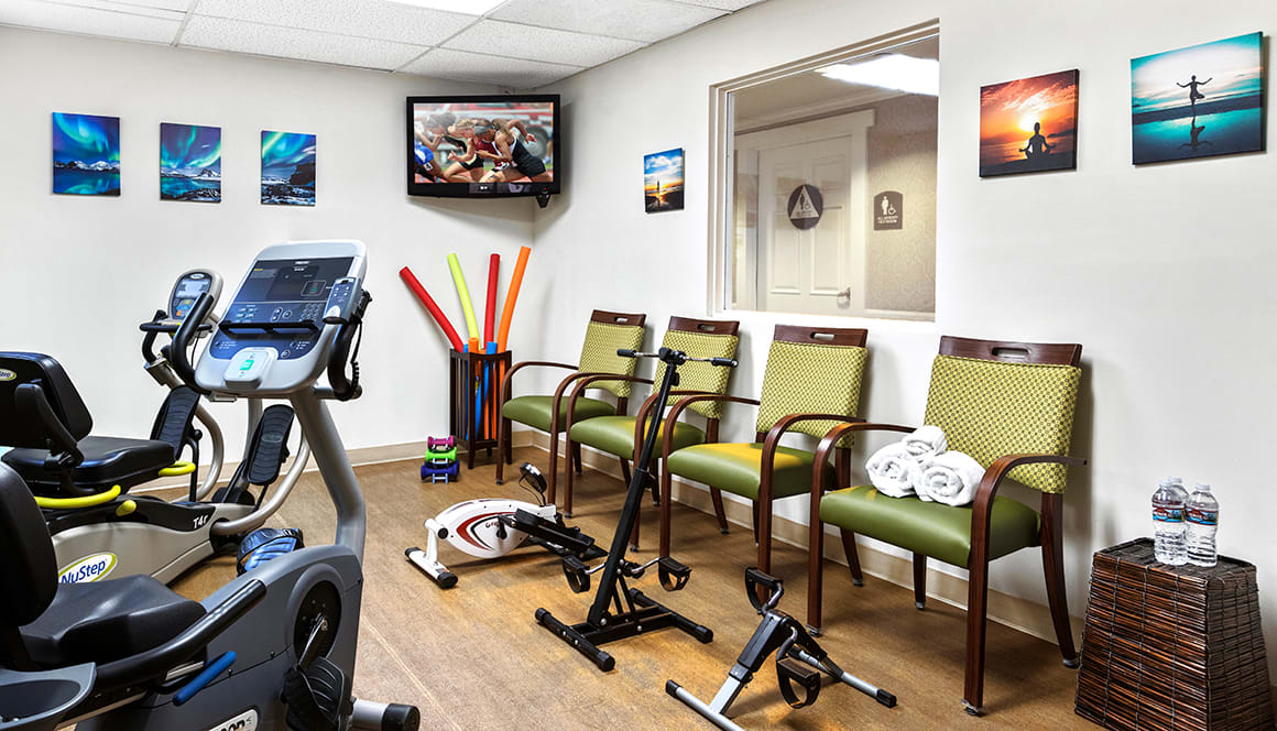 A waiting area with exercise equipment and seating, featuring a TV and decorative wall art.