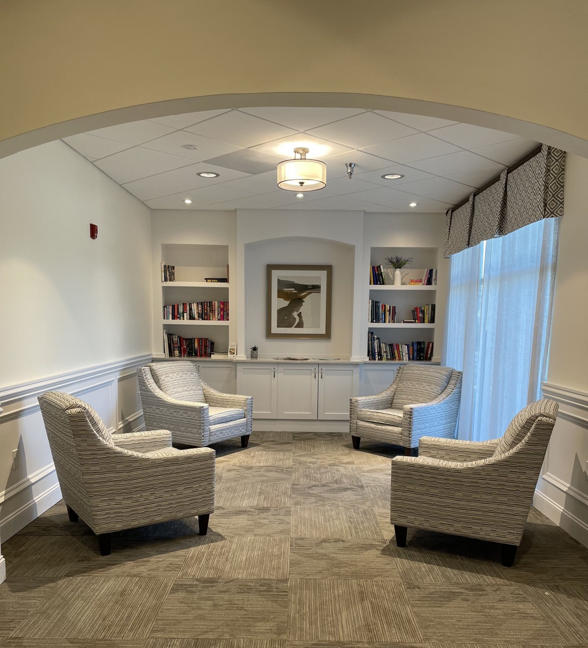 A cozy lounge area featuring four armchairs arranged in a circle, surrounded by bookshelves and illuminated by a chandelier.