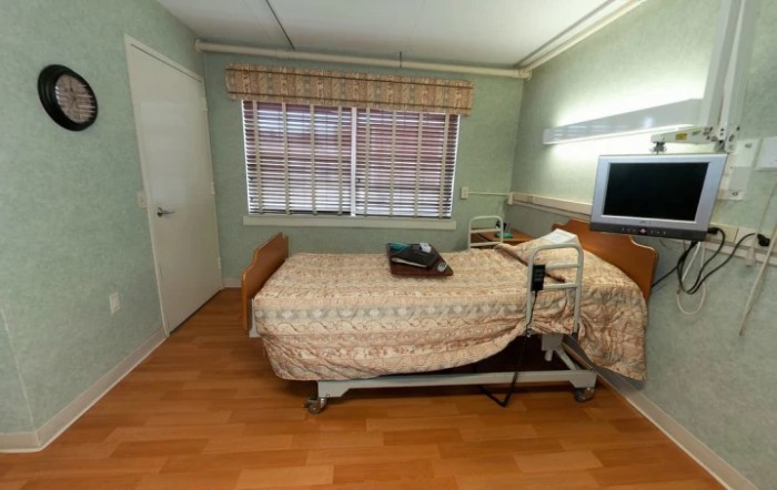 A hospital room with a single bed, television, and window.