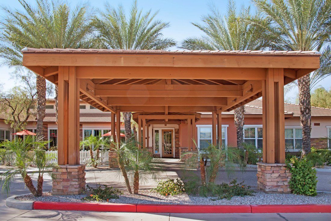 A building entrance with a wooden pergola surrounded by desert landscaping and palm trees.