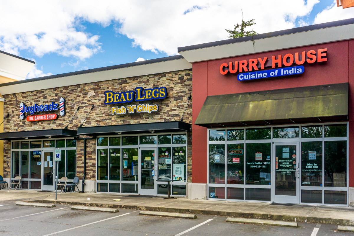 A view of a small shopping center featuring 'Beau Legs Fish & Chips' and 'Curry House Cuisine of India' with a parking area in front.
