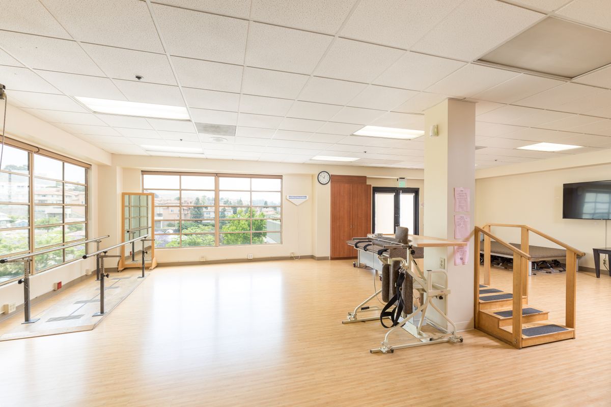 A spacious rehabilitation center with therapy equipment and large windows providing ample natural light.